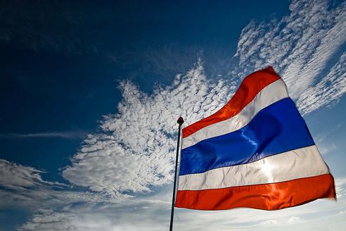Thai flag fluttering against a blue sky with white clouds